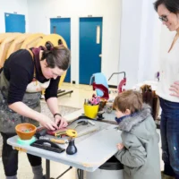 Une mère et son fils qui regarde une personne réparer un appareil dans le puits du Hall