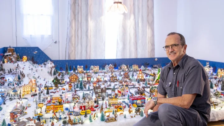 Monsieur Roger Couture assis près de son village miniature de Noël