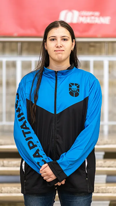 Une athlète de l'équipe de sport électronique pose sur les marches de l'escalier du hall d'entrée du Cégep de Matane pour sa photo d'équipe, vêtue de la veste bleue et noire des Capitaines.