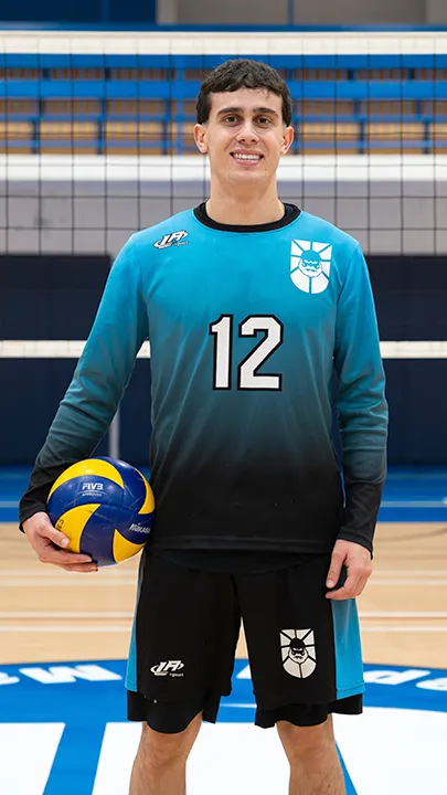 Dans un gymnase, devant un filet de volleyball installé sur un terrain omnisport, un athlète en tenue officielle des Capitaines pose avec un ballon de volleyball lors de la prise des photos officielles de l'équipe.