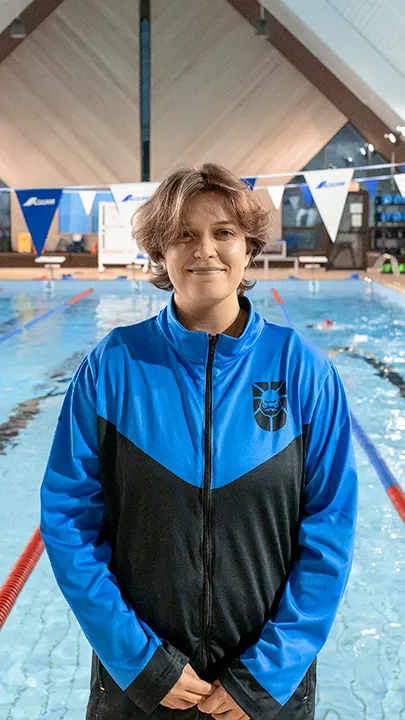 Une athlète des Capitaines, dans une piscine, sur le bord d'un bassin de natation, pose avec la tenue bleue et noire des Capitaines dans le cadre de la photo officielle de l'équipe collégiale de natation.