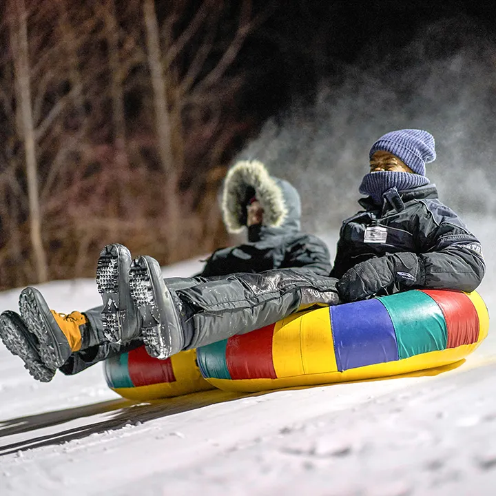 Deux personnes, emmitouflées dans des vêtements d'hiver, se cramponnent lors d'une glissade sur tube dans la forêt.