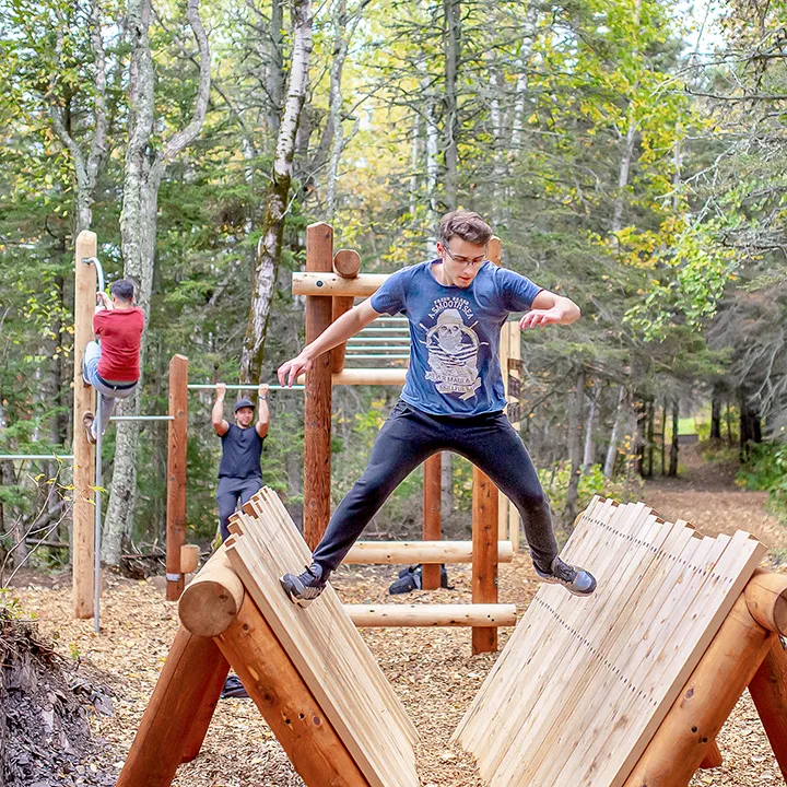 À l'extérieur, au cœur d'un boisé, trois étudiants pratiquent des exercices de remise en forme sur un parcours vitalité en bois installé au milieu des arbres.