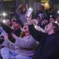 Dans le puits du hall du cégep, des membres du public emballés par la musique brandissent leur téléphone portable pour éclairer les personnes en train de chanter sur scène.